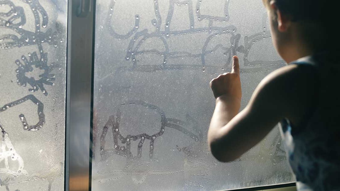 Gutt som tegner på kondens på vindu.